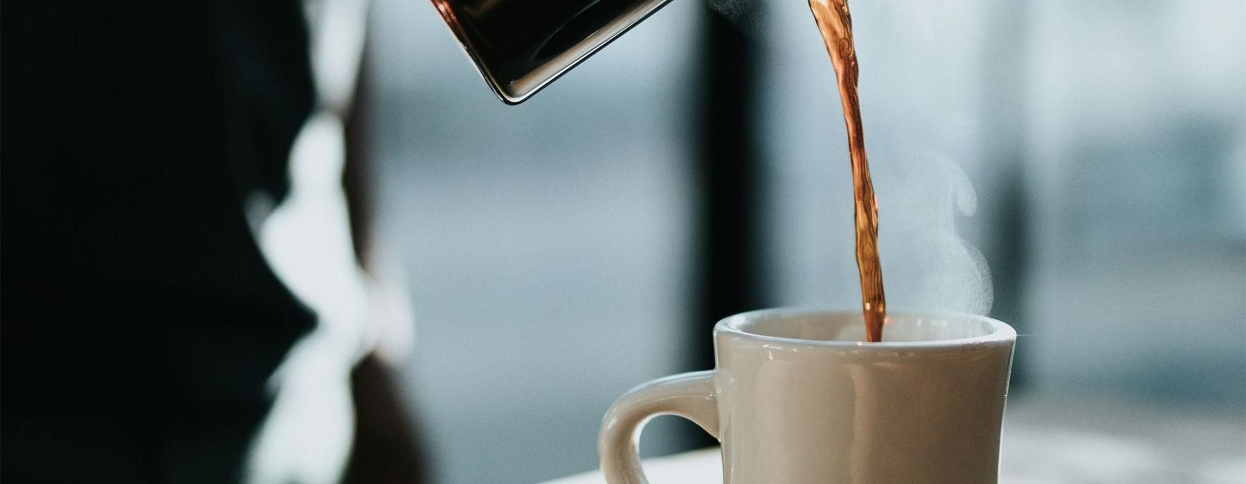 a person pouring a carafe of coffee into a cup