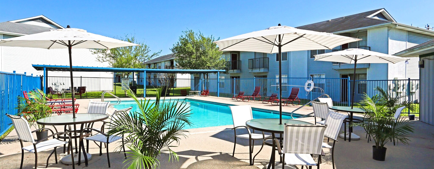 A pool with shaded tables and chairs surrounding around it